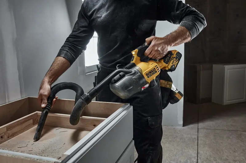 Personne nettoie la poussière d’un meuble en bois avec un aspirateur portatif DEWALT sans fil en chantier.