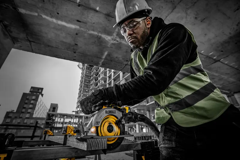 Une personne utilise une scie circulaire DEWALT DCS565NT sur un chantier, équipée et coupant du bois.