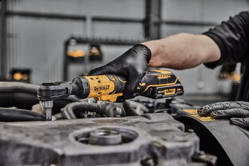 Une personne portant des gants noirs utilise une clé à cliquet sans fil DEWALT pour travailler sur un composant de moteur