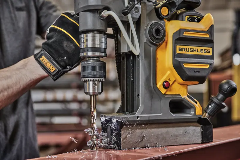 Une personne perce du métal avec une perceuse magnétique DEWALT brushless, générant des copeaux de métal.