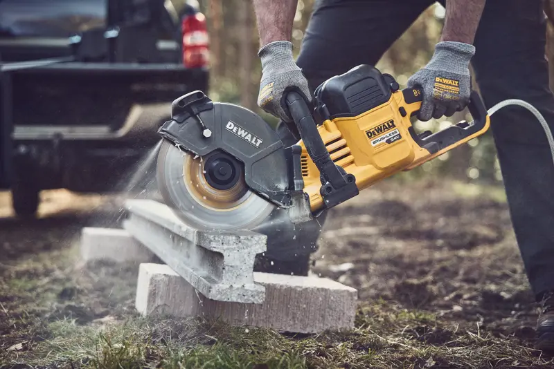 Scie DEWALT coupant du béton dehors, opérateur portant des gants pour sécurité.